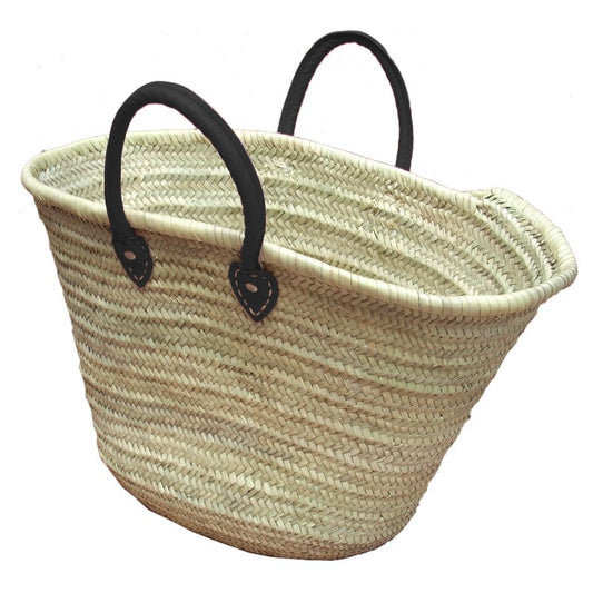 French straw beach basket with black leather handles against white background