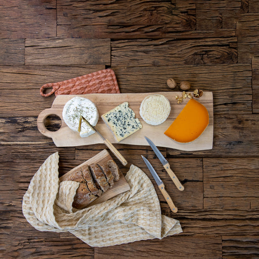 Acacia wood cheese board with four kinds of cheese, knives and bread