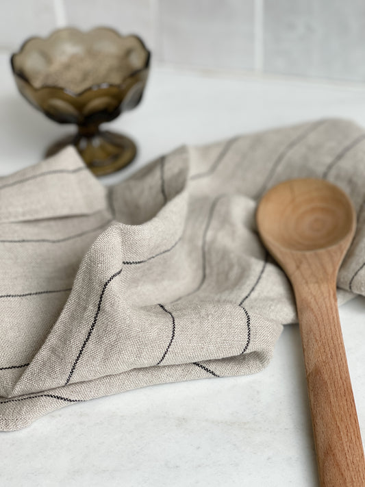 Natural linen kitchen towel with black stripe on countertop with wooden spoon