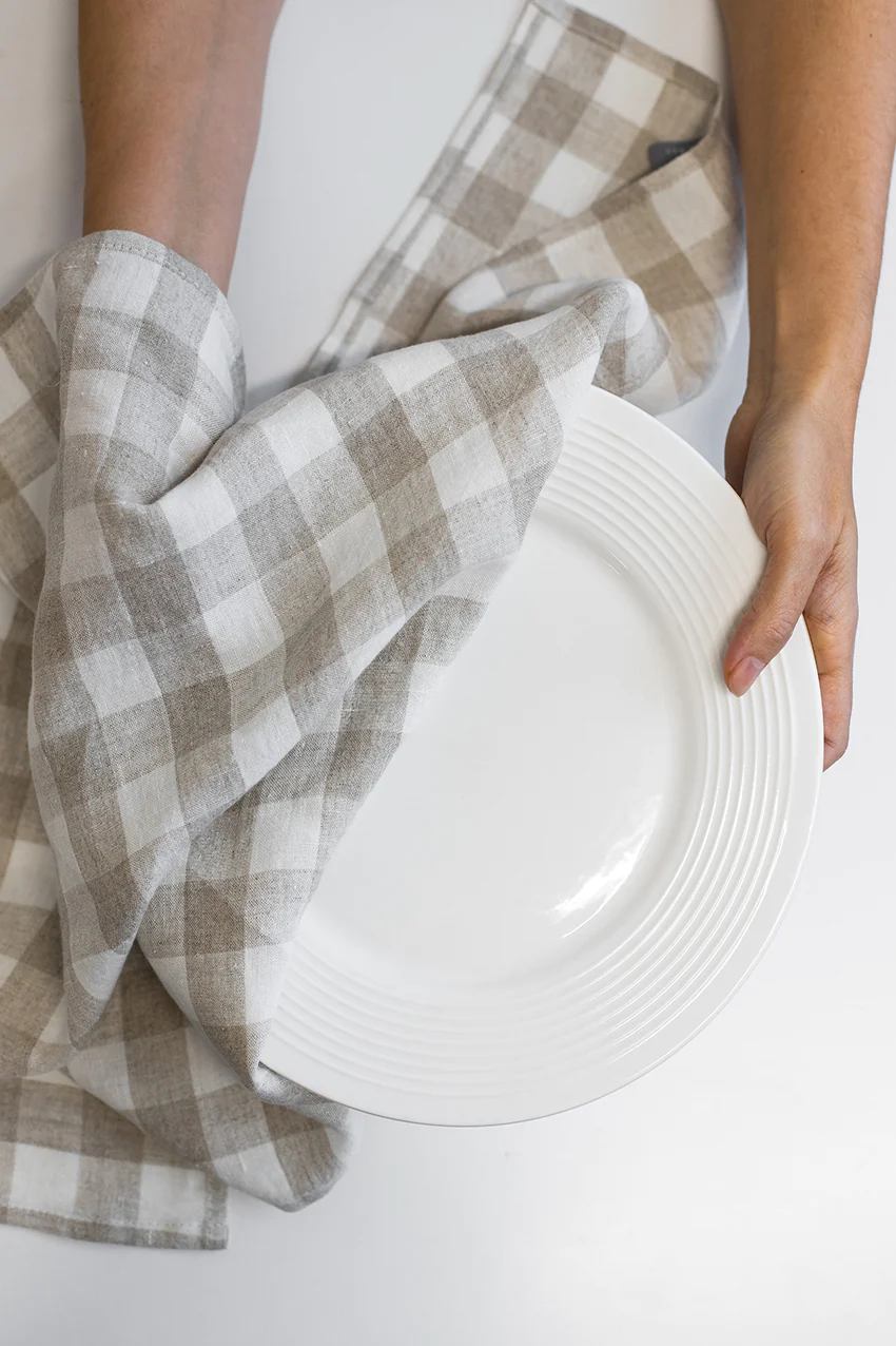 Hands drying a plate with ivory checkered kitchen towel from La Maison Baude